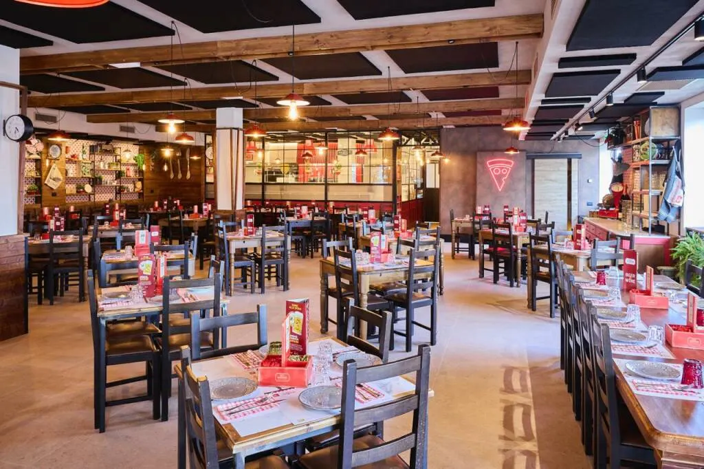 Sala con tavoli in legno e dettagli rossi nella nuova sede di Rosso Peperoncino